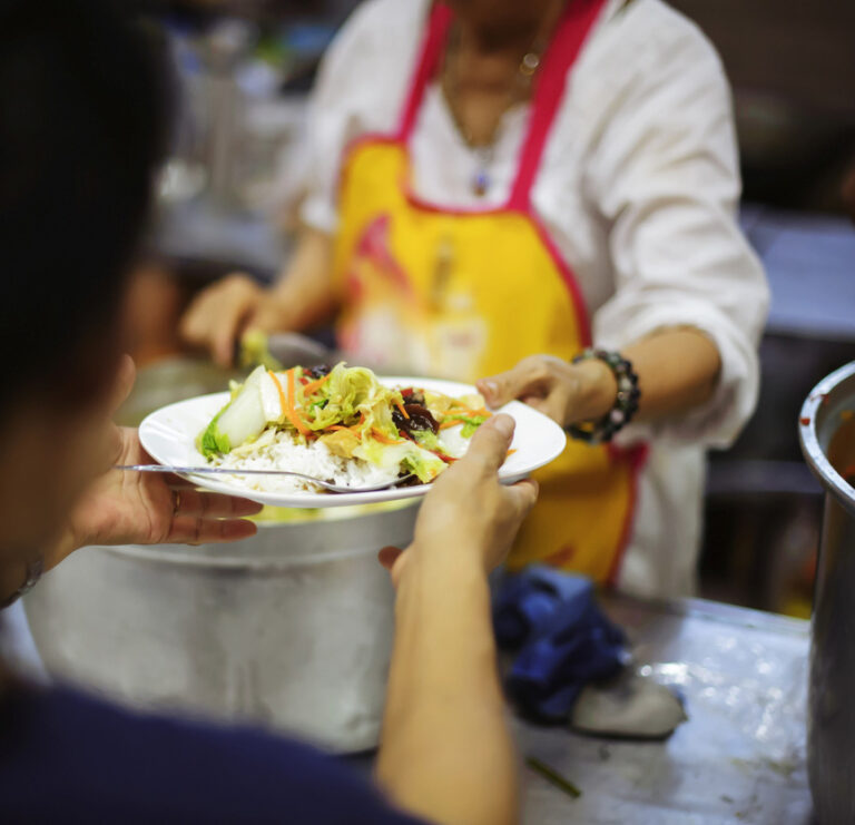 Une cuisinière donne une assiette avec un plat à une personne