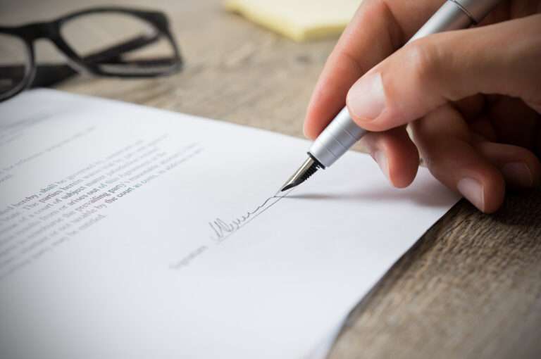 Une main signe un courrier avec un stylo.