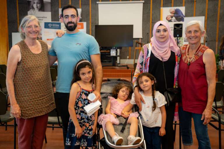 Une famille avec trois petites filles et des bénévoles posent lors d'une rencontre.