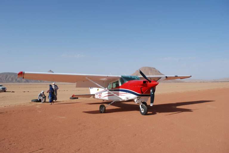 un avion rouge et blanc posé sur une base dans un milieu désertique