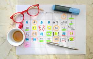 Un planner posé sur une table avec une tasse de caté, une paire de lunettes et des stylos