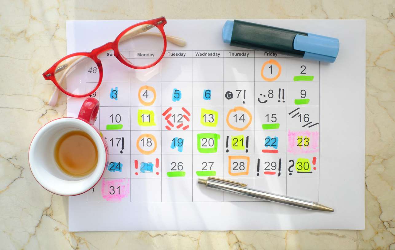 Un planner posé sur une table avec une tasse de caté, une paire de lunettes et des stylos